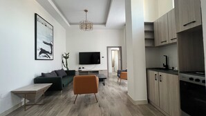 Moderni olohuone, jossa on sohva, sohvapöytä ja televisio. Keittiöalueella on kaappeja ja liesi.