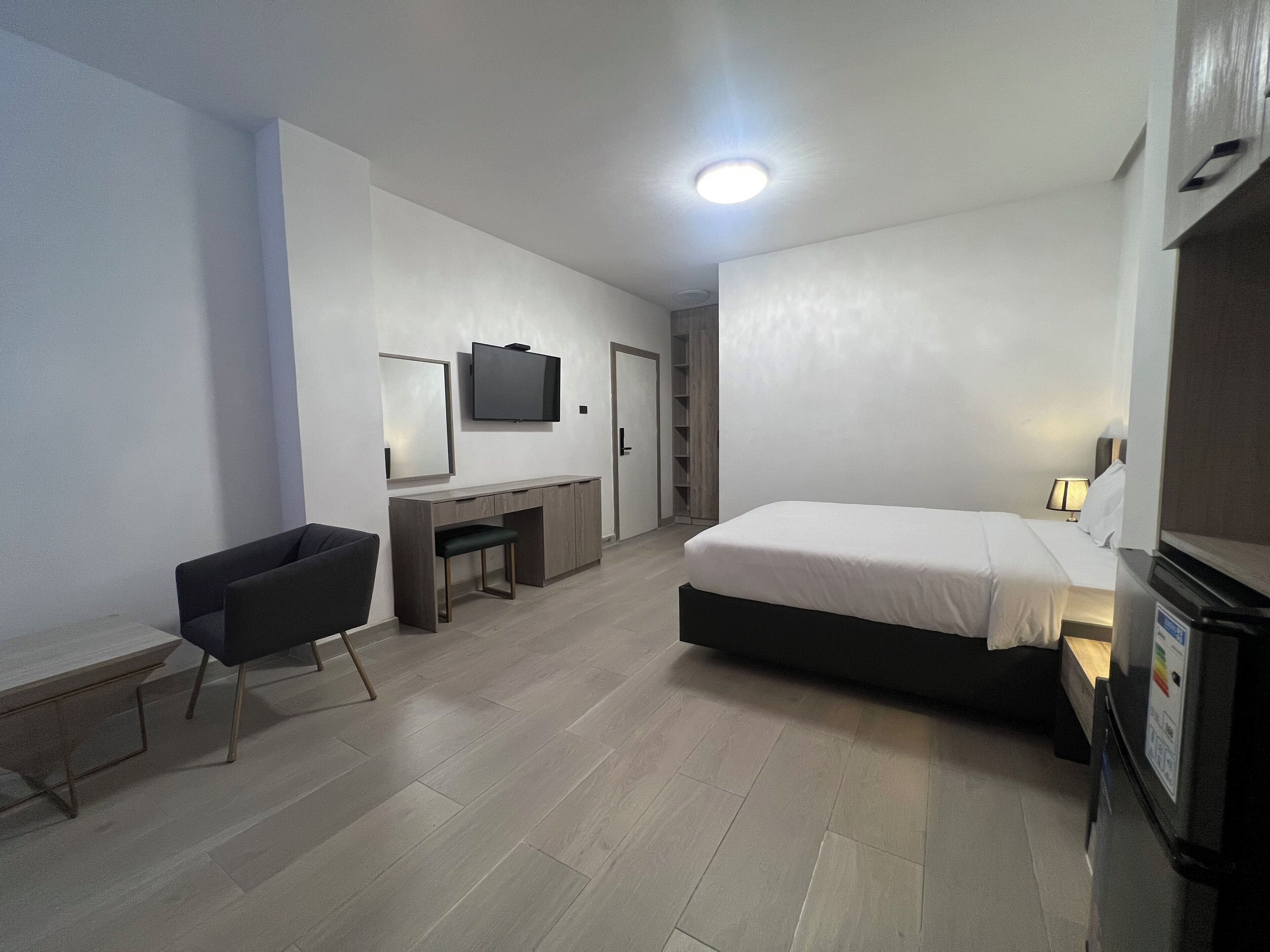 A modern hotel room with a bed, a desk, a chair, a television, and a wardrobe.