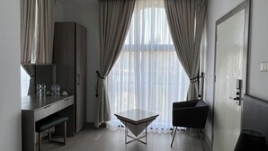 Moderni hotellihuone, jossa on pelkistetty sisustus. Huoneeseen kuuluu työpöytä, tuoli, penkki ja suuri ikkuna, jossa on läpikuultavat verhot.
