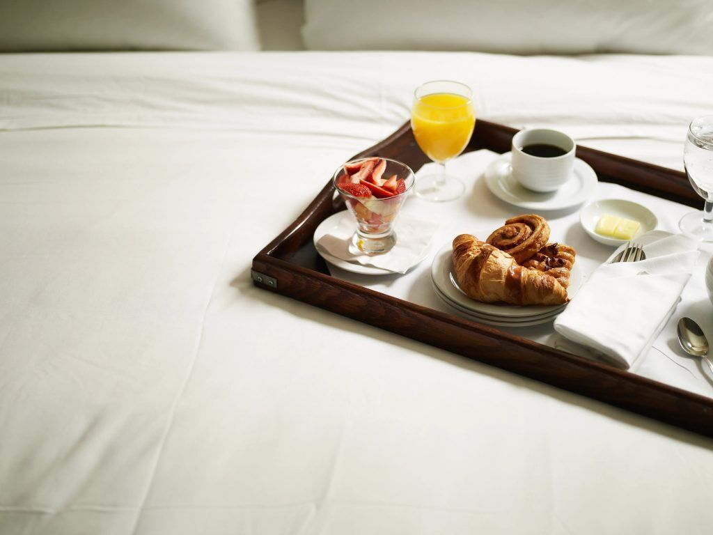 Bandeja de desayuno en una cama con cruasanes, un vaso de zumo de naranja, una taza de café y un bol pequeño de mantequilla.