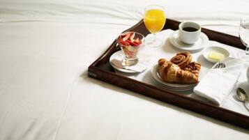 Bandeja de desayuno en una cama con cruasanes, un vaso de zumo de naranja, una taza de café y un bol pequeño de mantequilla.