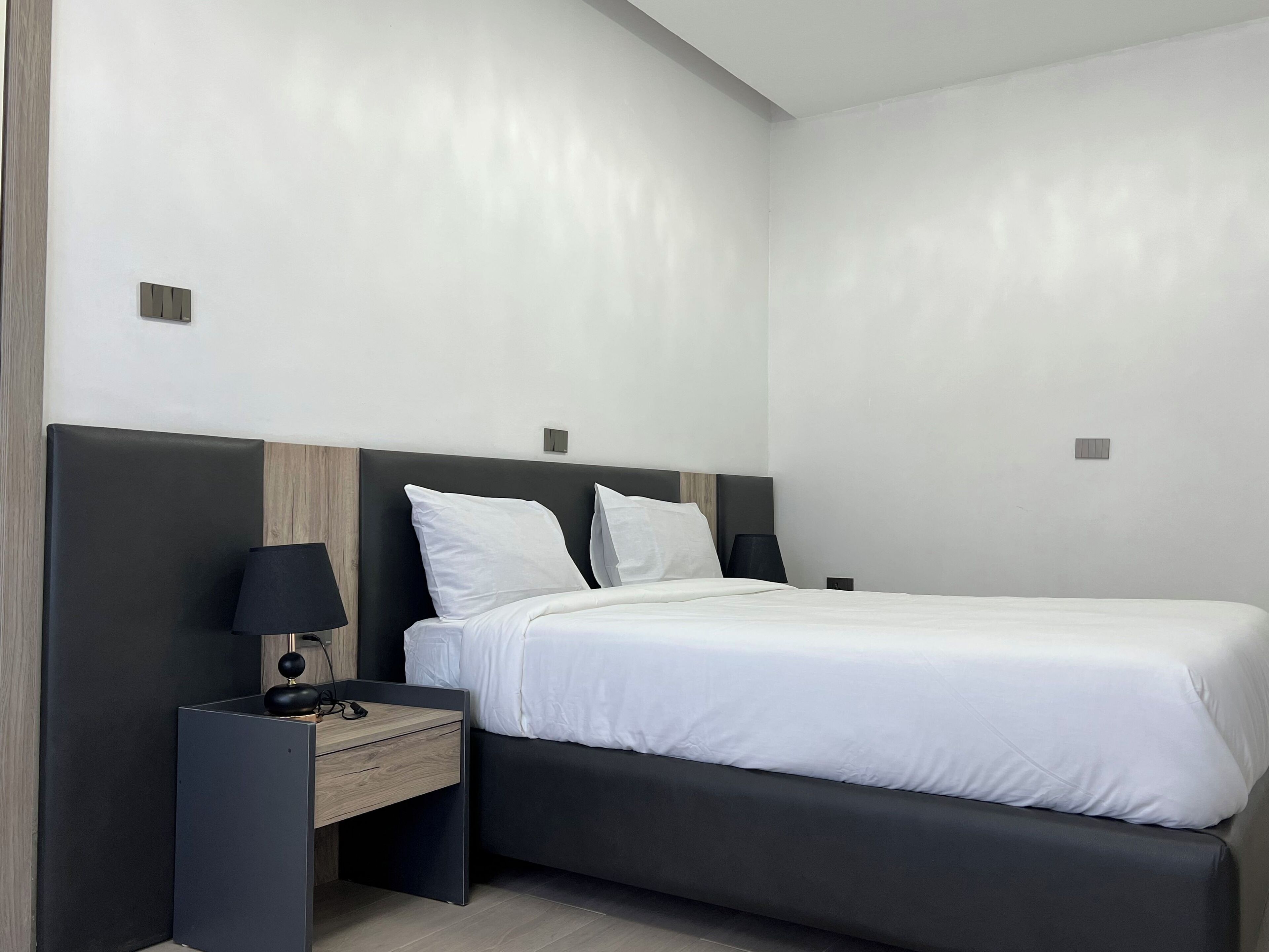 Een moderne hotelkamer met een bed, een nachtkastje met een lamp en een houten paneel aan de muur.