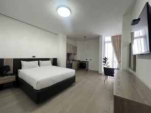 A modern hotel room with a large bed, a desk, a kitchenette, and a TV mounted on the wall. - Elsol Hotel (Addis Ababa)