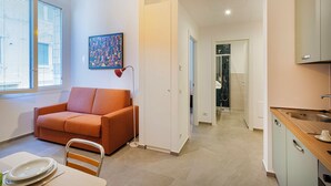 A modern living room with a sofa, a dining table with plates, a painting on the wall, and a kitchen area with cabinets and a sink. - Carignano Sweet Home by Wonderful Italy (Genoa)
