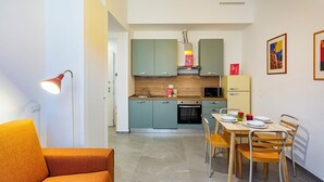 A modern kitchen with teal cabinets, a microwave, and a yellow refrigerator. There is a dining table with chairs and a red lamp on the left. - Carignano Sweet Home by Wonderful Italy (Genoa)