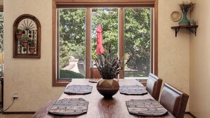 Une salle à manger avec une grande fenêtre, un vase contenant des plantes séchées et un élément décoratif mural.