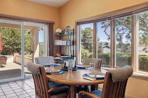 A dining area with a round table, chairs, and a view through large windows.