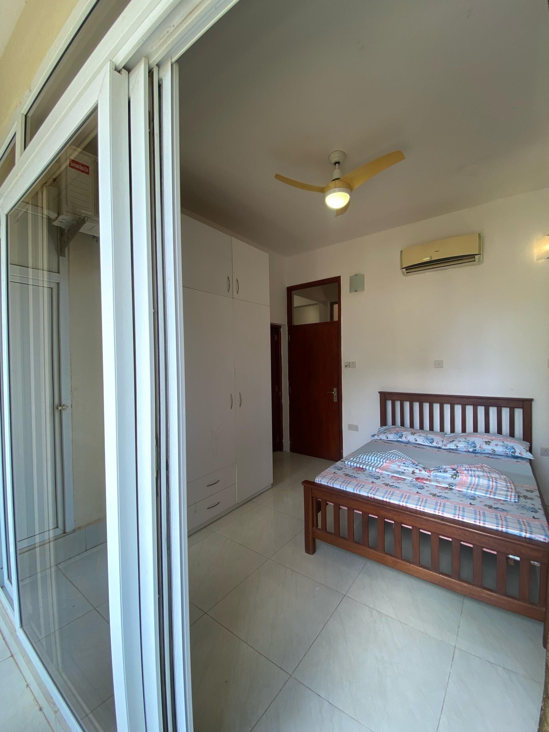 A bedroom with a bed, a ceiling fan, an air conditioning unit, and a wardrobe.