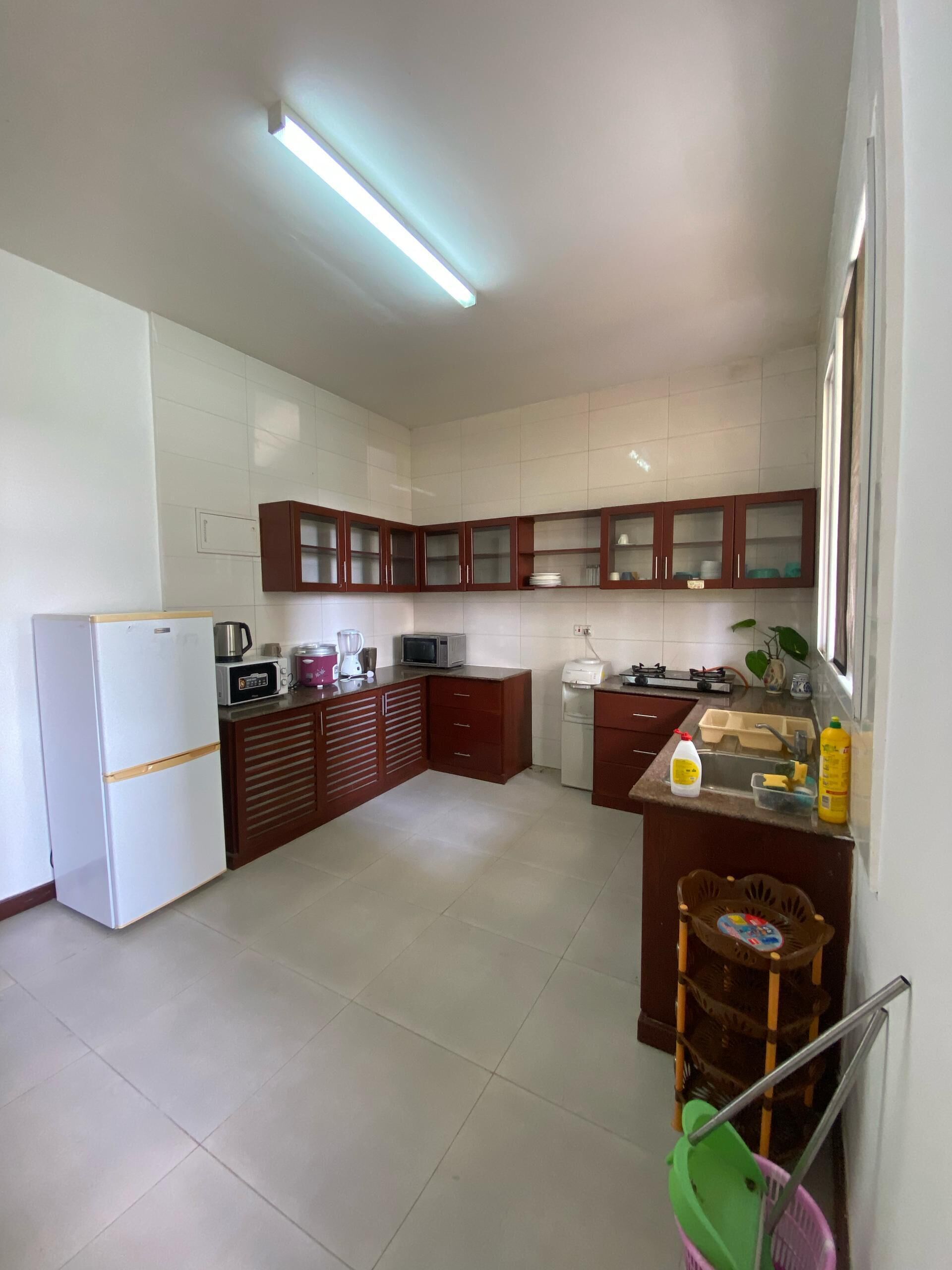 Una cocina compacta con armarios blancos, un refrigerador, microondas y un lavamanos.