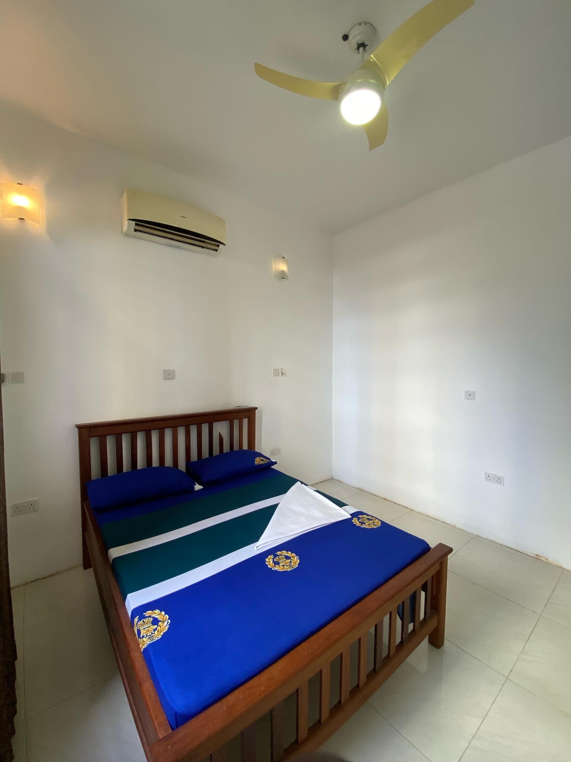 A bedroom with a wooden bed, a ceiling fan, an air conditioner, and a wall-mounted light.