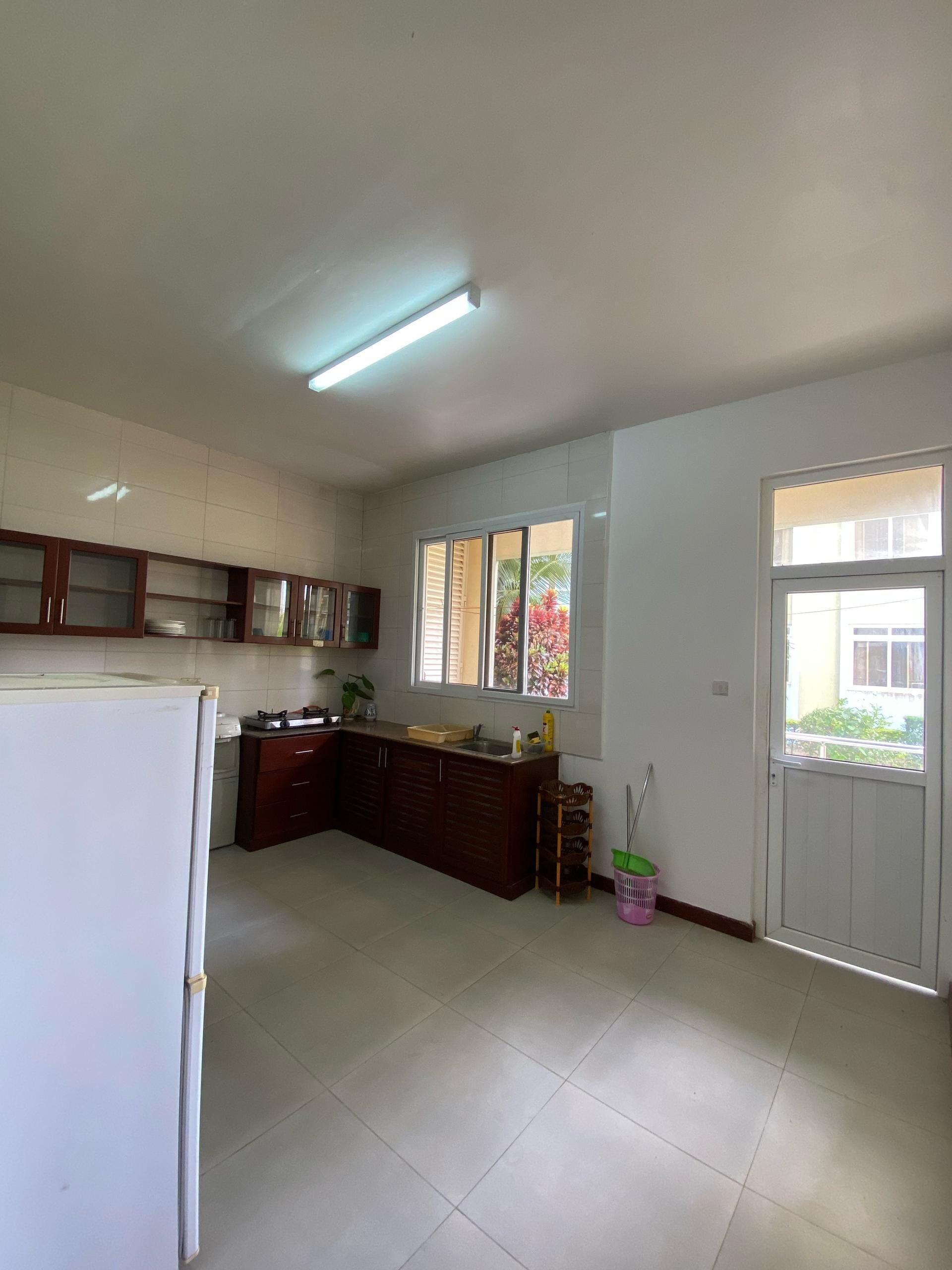 Una cocina con refrigerador, armarios, un lavamanos y una ventana con persianas.