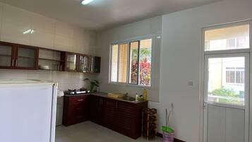 Una cocina con refrigerador, armarios, un lavamanos y una ventana con persianas.