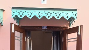 A wooden door with a number plate indicating room 102, leading to a tiled floor and a doormat.