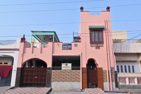 Um edifício rosa com duas entradas em arco e uma placa indicando Ardas Villa Bikaner.