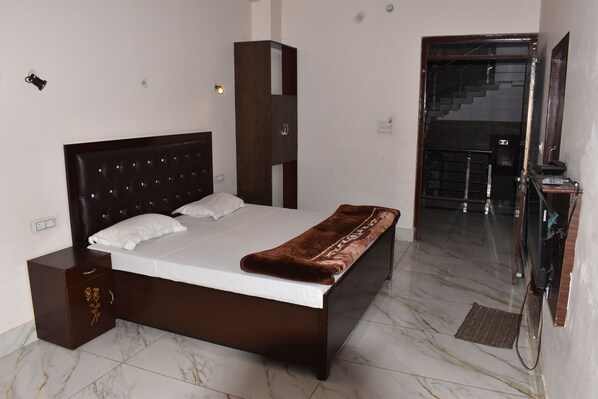 A bedroom with a large bed, a nightstand, a wardrobe, and a staircase leading to an upper floor. - Hotel Prakash Paradise (Pilibhit)