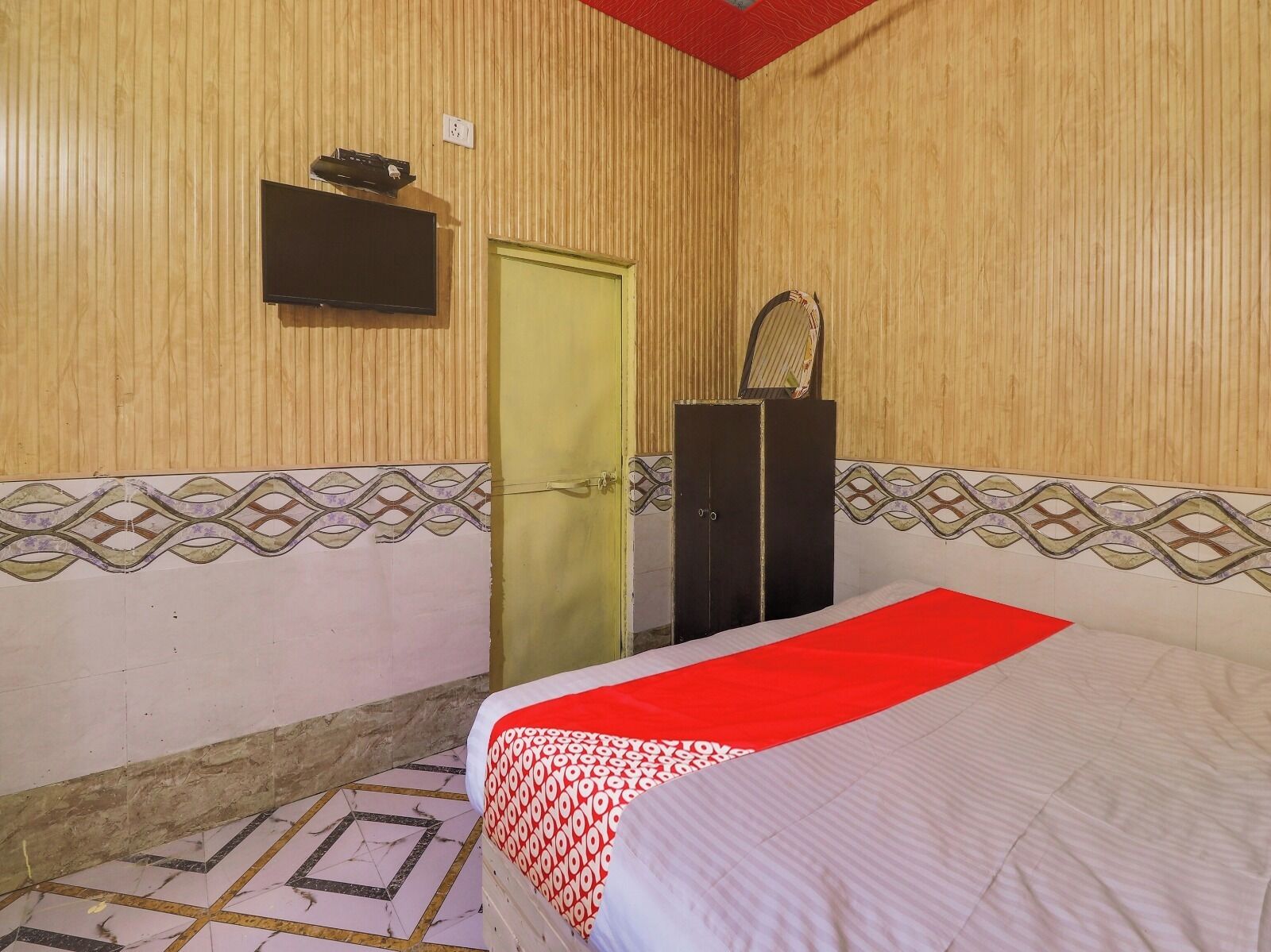 A hotel room with a bed, a wardrobe, a television mounted on the wall, and a door.
