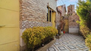Ένα στενό σοκάκι με πλακόστρωτο δρόμο, μια κίτρινη πόρτα και έναν τοίχο από τούβλα με ένα διακοσμητικό σχέδιο.