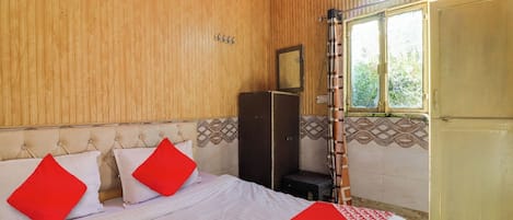 A bedroom with a bed, pillows, a wardrobe, a window, and a door.