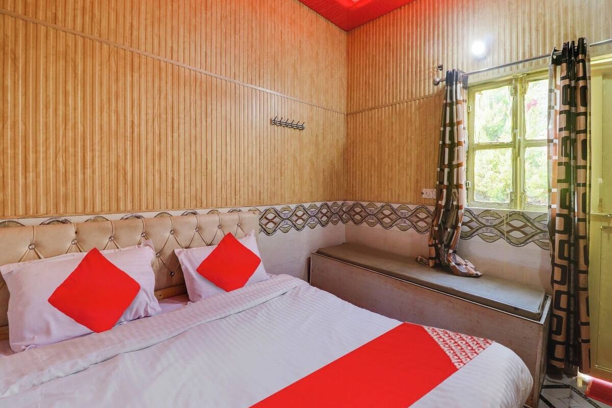 A bedroom with a bed, a bench, a window with curtains, and a wooden wall.
