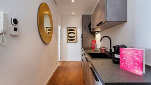 Een moderne hotelgang met een houten vloer, een grote spiegel, een telefoon en een kitchenette met een koffieapparaat.