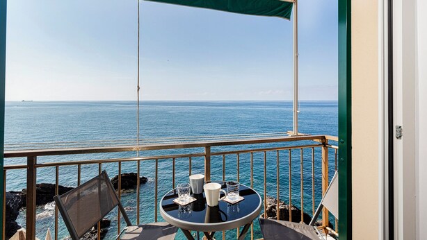 Een balkon met een tafel, stoelen en uitzicht op zee.