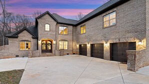 Une maison à deux étages, construite en briques, avec une grande allée, plusieurs portes de garage et une entrée bien éclairée.