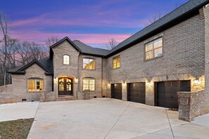 A two-story brick house with a large driveway, multiple garage doors, and a well-lit entrance.