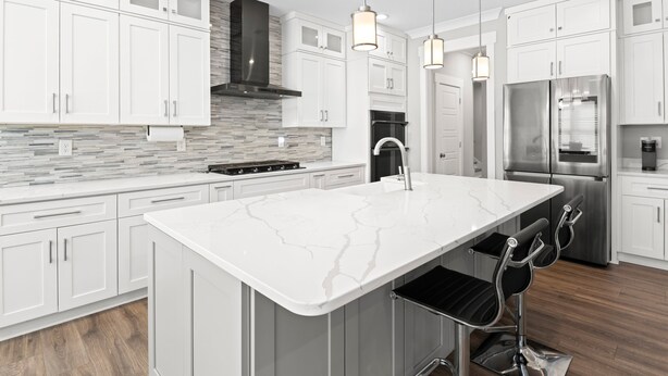 Une cuisine moderne avec des meubles blancs, un îlot en marbre, des appareils électroménagers en acier inoxydable et des luminaires suspendus.