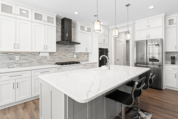 A modern kitchen with white cabinetry, a marble island, stainless steel appliances, and pendant lighting.