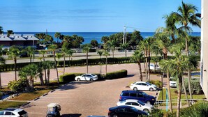 A parking lot with several cars, palm trees, and a view of the ocean.