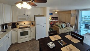 A compact kitchen with white appliances, a dining area with a table set for two, and a view of the ocean through large windows.