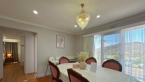 Une salle à manger agrémentée d’un lustre, une table dressée pour quatre personnes et une vue sur un paysage montagneux, visible à travers de grandes fenêtres.