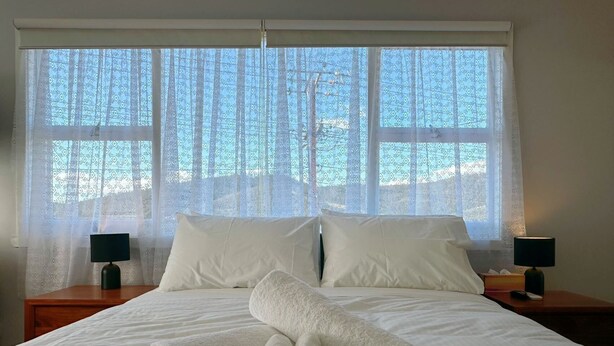 Une chambre d’hôtel avec un grand lit, deux tables de chevet avec des lampes et une vue sur les arbres à travers des rideaux à motifs.