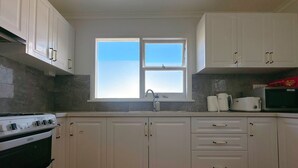 Une cuisine avec des meubles blancs, une fenêtre, un évier, une cuisinière et un four à micro-ondes.