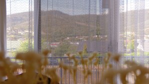Une vue à travers une fenêtre munie d’un moustiquaire, qui révèle un paysage avec des bâtiments et de la végétation.