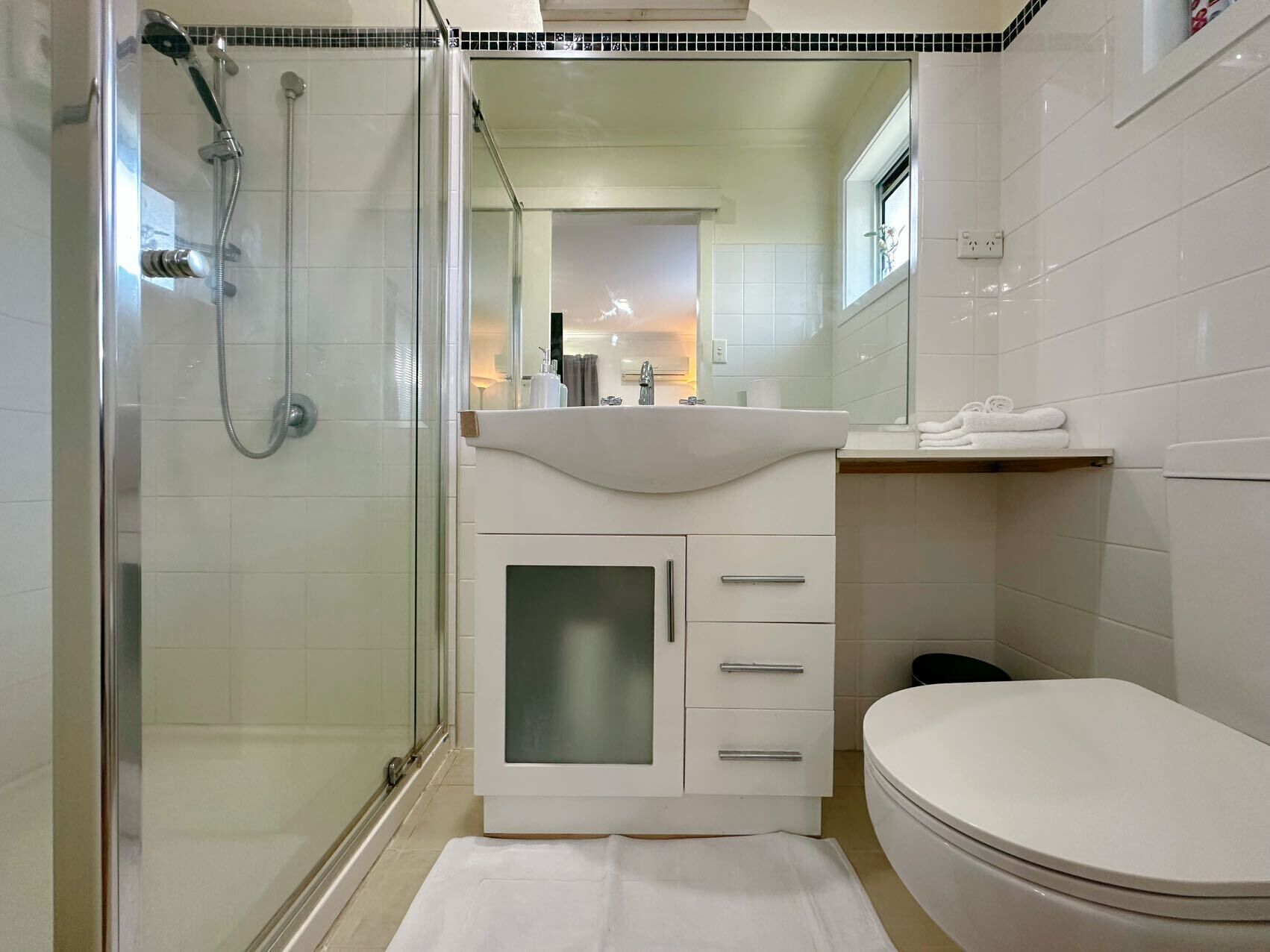 A bathroom with a glass shower enclosure, a white sink with a vanity, and a toilet.