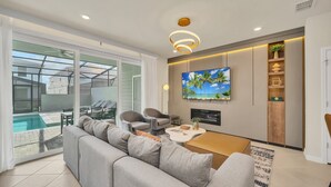 A modern living room with a grey sofa, two armchairs, a coffee table, and a TV mounted on the wall.
