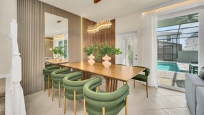 A modern dining area with a wooden table, green upholstered chairs, and a decorative light fixture.