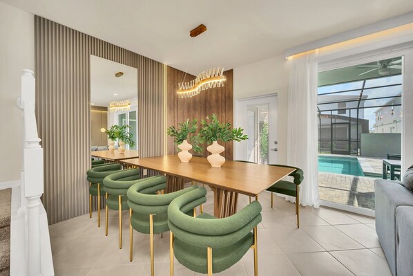 Un espace repas moderne avec une table en bois, des chaises à revêtement vert et un luminaire décoratif.