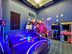 A room with a pool table, arcade games, and a neon-lit gaming setup.