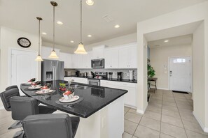 A modern kitchen with a central island, white cabinets, stainless steel appliances, and pendant lighting.
