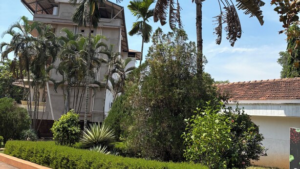 Un edificio con techo de tejas, rodeado de setos cuidados y palmeras.