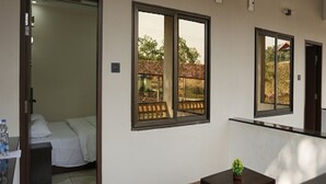 Habitación de hotel con cama, una mesita con una planta y amplias ventanas que dan a un espacio exterior cercado.