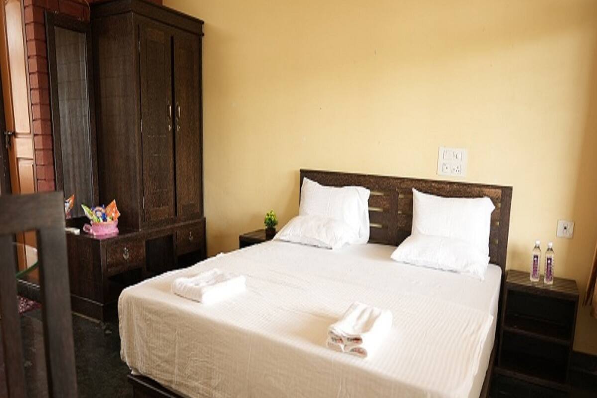 Una cama bien hecha con sábanas y toallas blancas, un armario de madera y una mesita de noche con una planta y botellas.