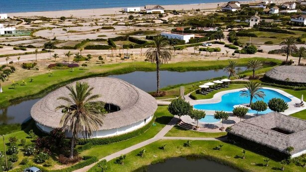 Un resort con un edificio circular, una piscina y una playa al fondo.
