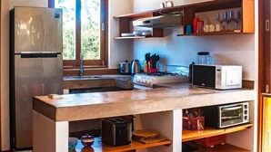 Una cocina compacta con refrigerador, microondas, tostadora y un horno pequeño. Hay una ventana que proporciona luz natural y una encimera de madera.