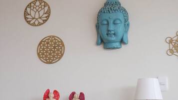 A room with a Buddha head sculpture, decorative wall hangings, and a lamp on a wooden table.
