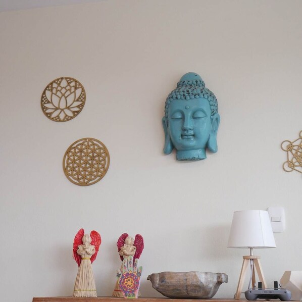 Una habitación con una escultura de cabeza de Buda, adornos colgantes en la pared y una lámpara sobre una mesa de madera.