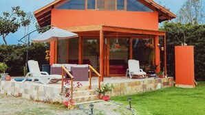Una casa moderna de dos pisos con fachada roja, grandes ventanales y un patio cubierto con mobiliario exterior.