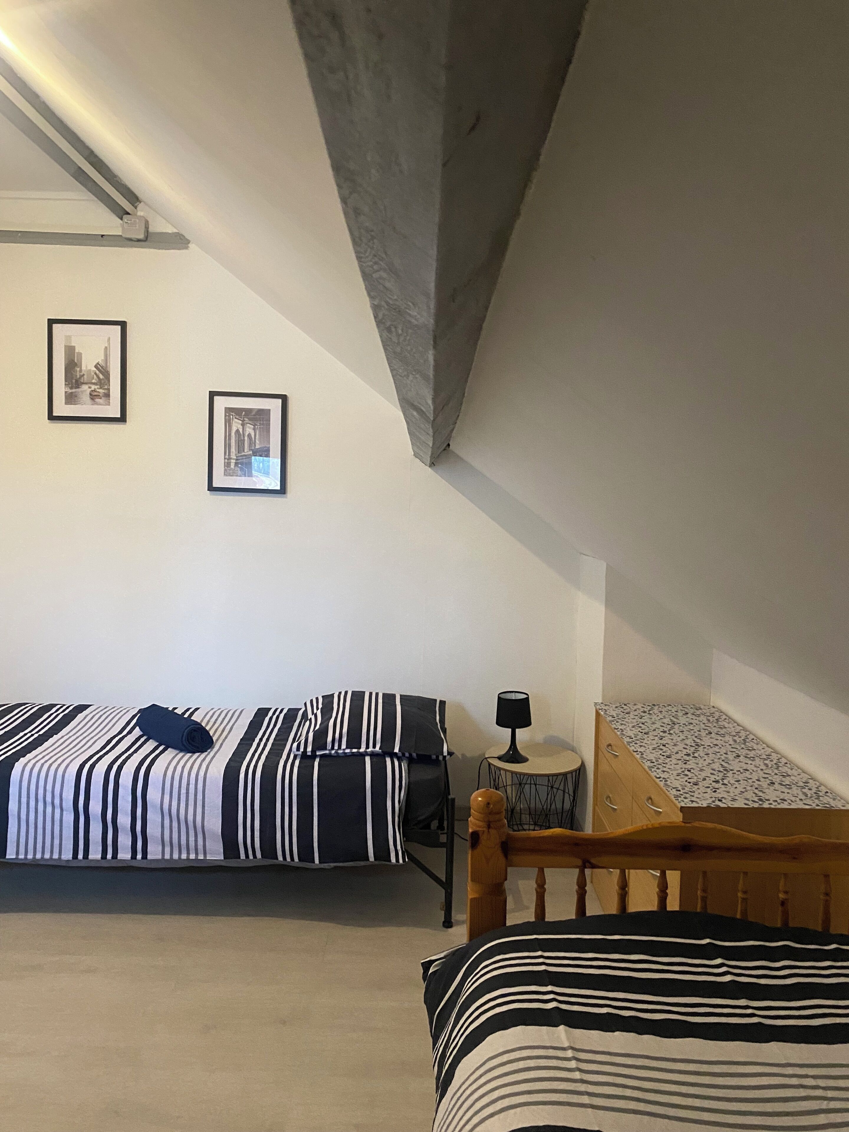 Une chambre à coucher avec un lit, une petite table sur laquelle se trouve une lampe, et deux tableaux encadrés accrochés au mur.